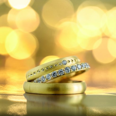 Close-up van drie gouden trouwringen met diamanten op een gouden achtergrond, perfect voor een luxe en stijlvolle bruiloft.