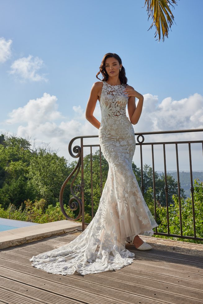 Bruid poseert aan het zwembad met groene bergen in de achtergrond. Ze heeft een witte bruidsjurk aan met een mooie halslijn.