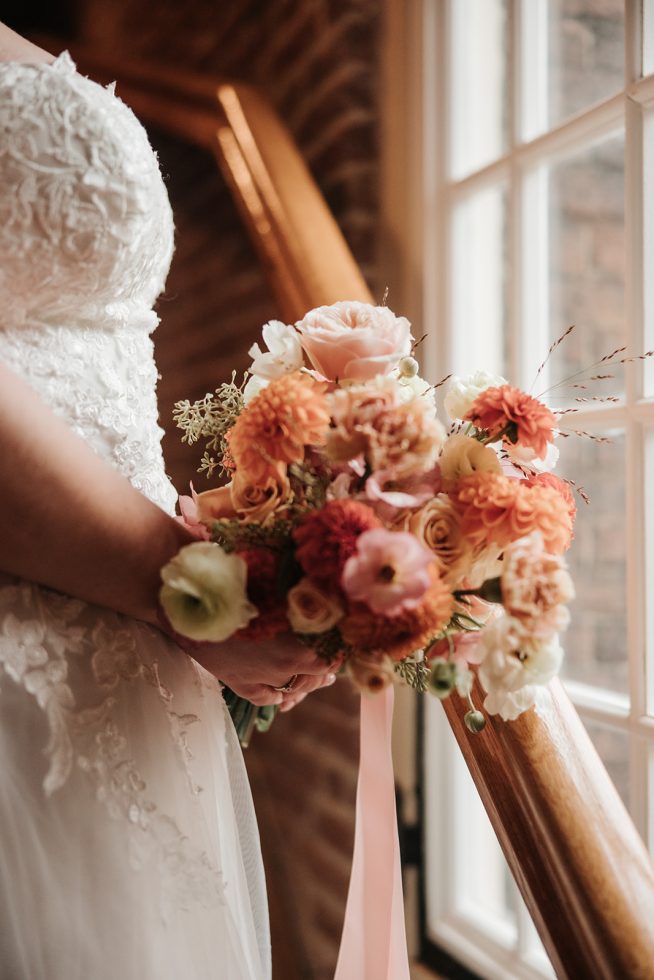 Close-up van een romantisch bruidsboeket met pastel- en aardetinten, vastgehouden door de bruid bij het raam van Hotel Arsenaal in Delft.