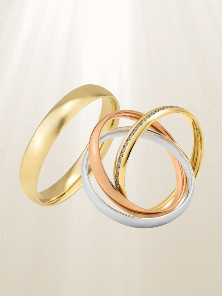 Collectie trouwringen in geelgoud, roségoud en witgoud, met en zonder diamanten, op een lichte achtergrond met stralend licht.