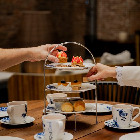 High tea in Hotel Arsenaal in Delft. Twee handen pakken iets van de etagère. Er liggen borden en kopjes bij in Delfts blauwe kleuren.