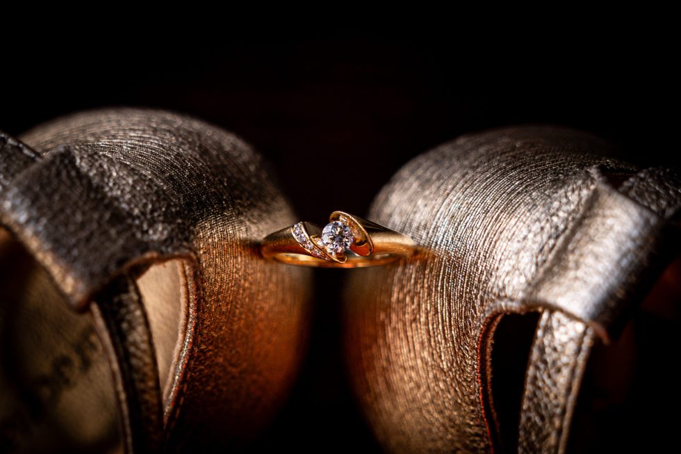 Verlovingsring tussen gouden trouwschoenen in romantisch licht.