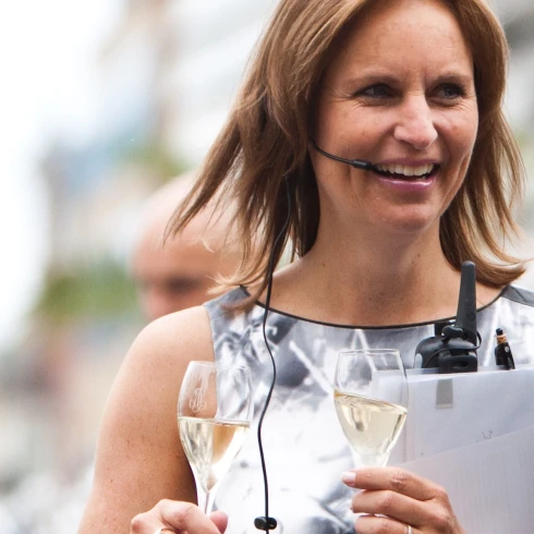 Astrid Blaauw weddingplanner in stijlvolle jurk met headset, twee champagneglazen en documenten in de hand.