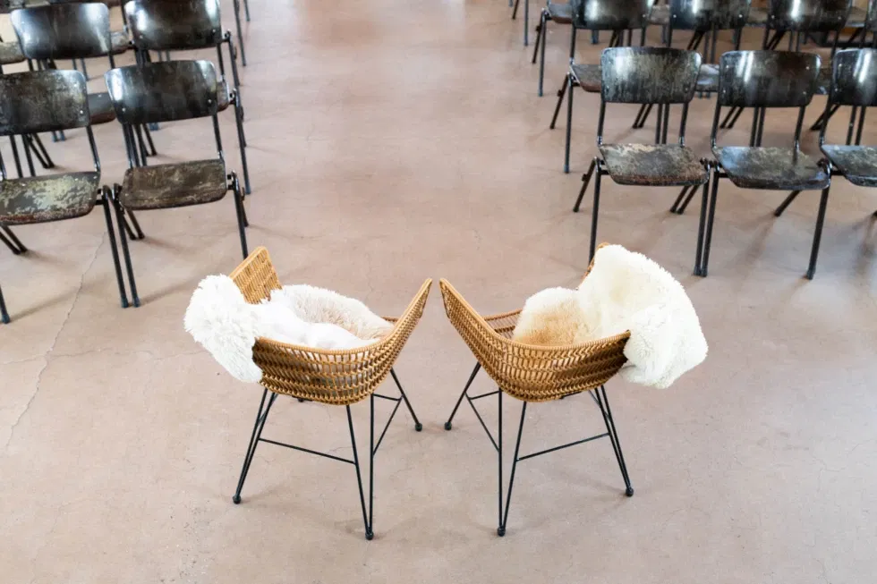 Ceremonie-opstelling met rotan stoelen en schapenvachtjes voor bruidspaar – industriële trouwlocatie met karakter en vintage sfeer.