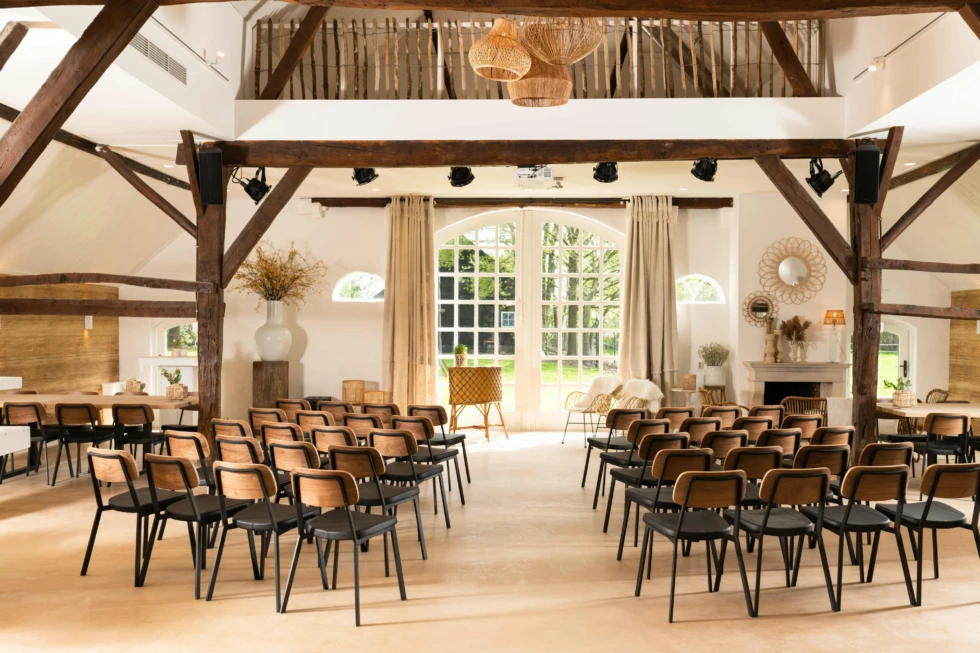 Lichte ceremonieruimte van De Veenderhoeve met houten balken, grote ramen en warme styling – moderne landelijke trouwlocatie met authentiek karakter.