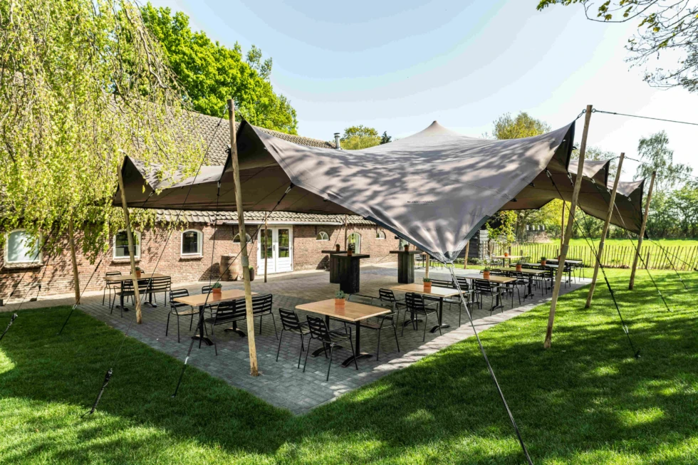 Buitenlocatie van De Veenderhoeve met stretchtent, terrastafels en uitzicht op het groen – zomerse trouwsetting met landelijke charme.