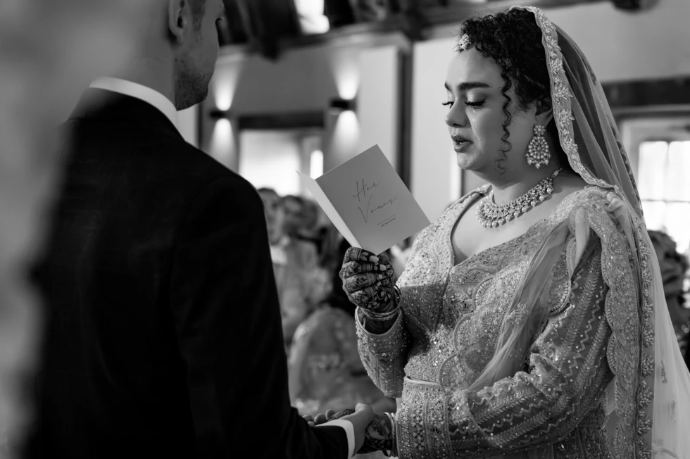 Emotionele bruid leest haar geloften voor tijdens multiculturele bruiloft – traditionele bruidsjurk met henna en sieraden in intiem trouwmoment.