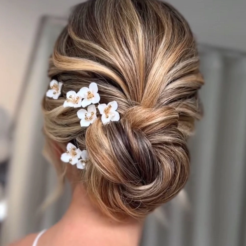 Elegant opgestoken kapsel met vlechtaccent en witte bloemenhaarspelden met gouden details.