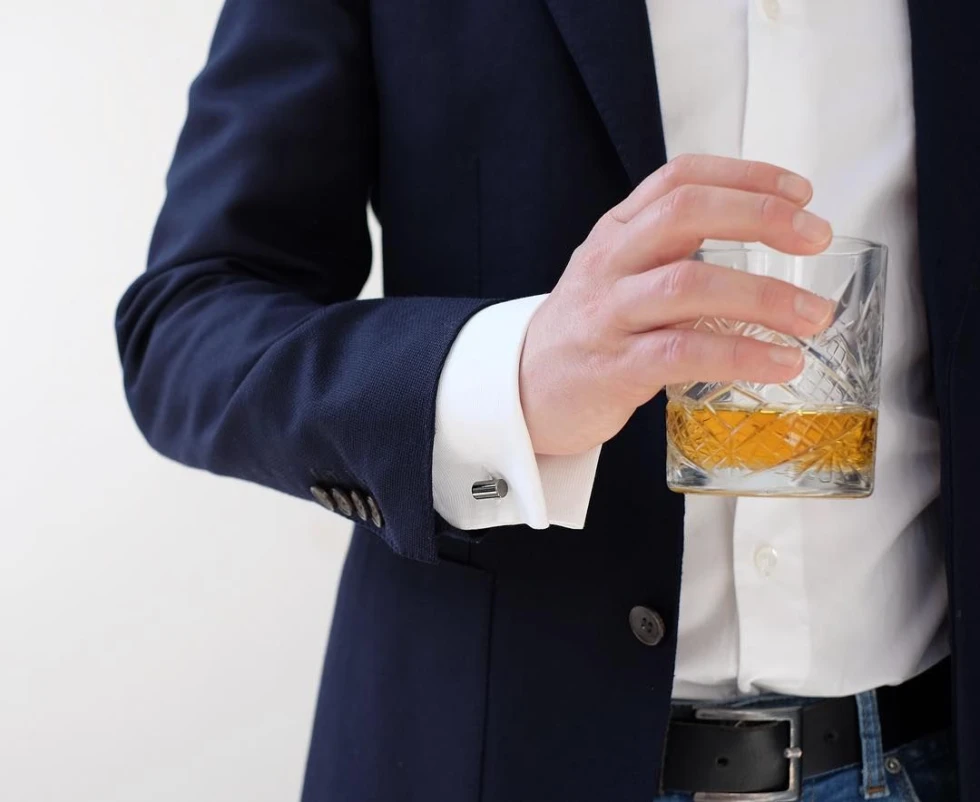 Man in donkerblauw colbert met whiskyglas en zilveren manchetknopen