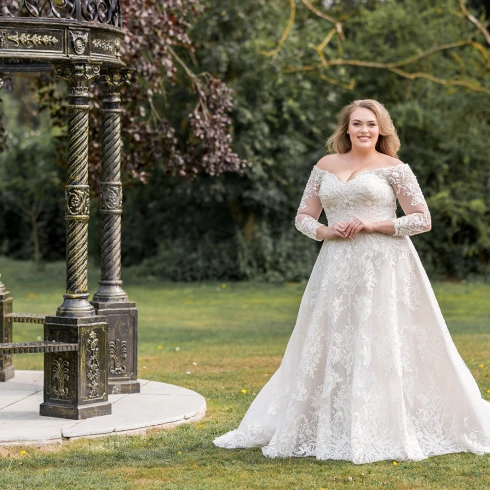 Romantische plus size trouwjurk met kant en lange mouwen – elegante bruidsmode voor curvy bruiden in een sprookjesachtige tuinsetting.