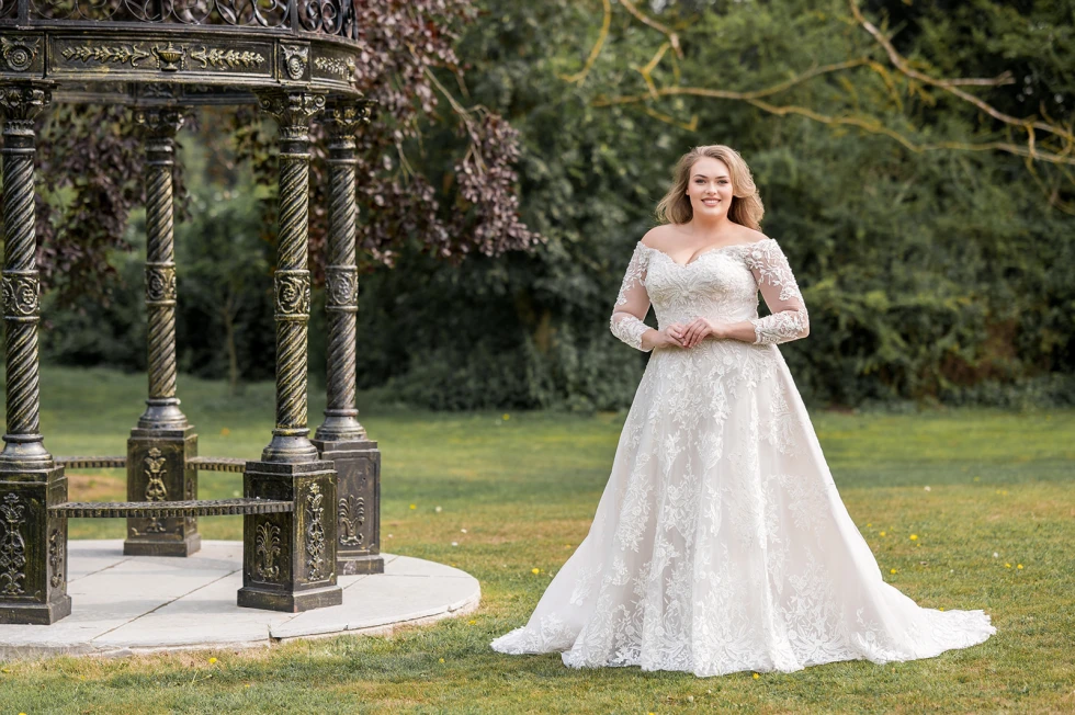 Romantische plus size trouwjurk met kant en lange mouwen – elegante bruidsmode voor curvy bruiden in een sprookjesachtige tuinsetting.