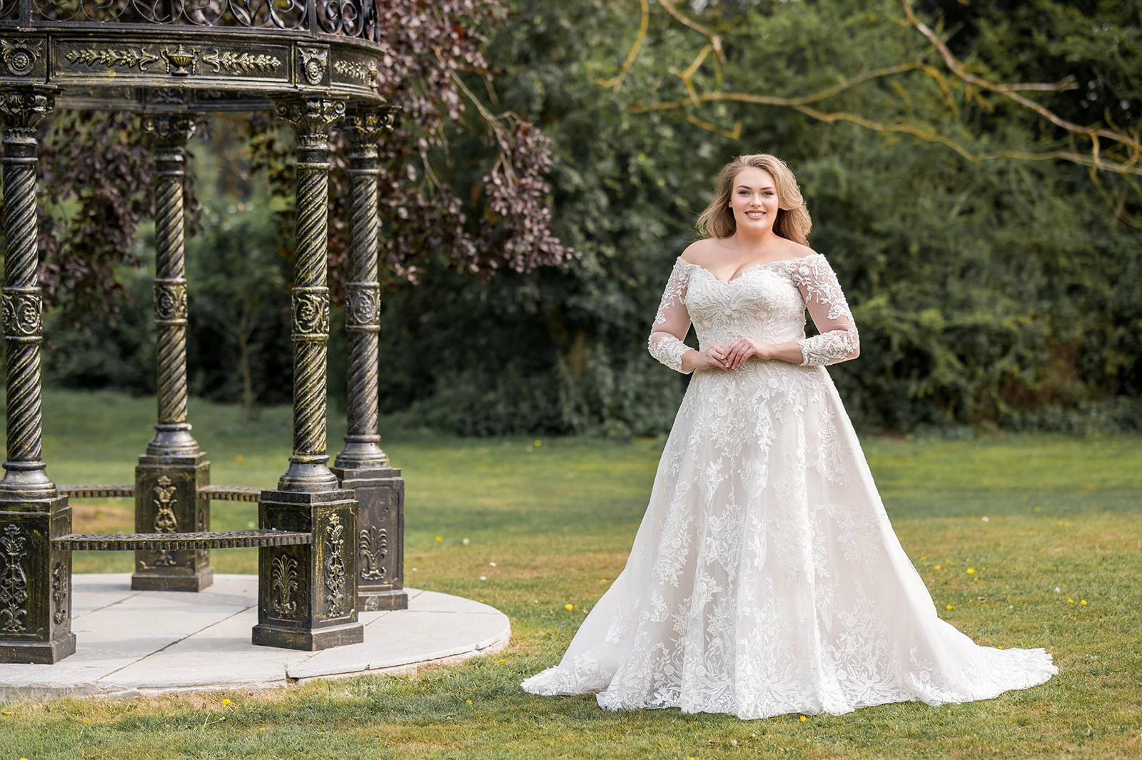 Romantische plus size trouwjurk met kant en lange mouwen โ elegante bruidsmode voor curvy bruiden in een sprookjesachtige tuinsetting.