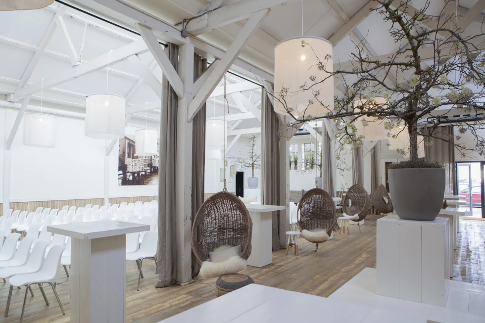 Deze ruimte van Het Oude Magazijn combineert industriële charme met huiselijke details zoals rotan schommelstoelen, witte accenten en houten vloeren. Perfect voor een ontspannen moment tijdens de trouwdag, of als sfeervolle plek voor een ceremonie of borrel.