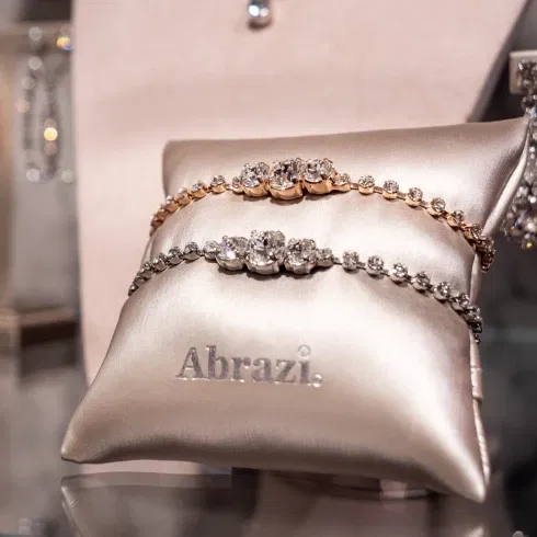 Twee sprankelende armbanden van Abrazi gepresenteerd op een satijnen kussen in een luxe vitrinekast.