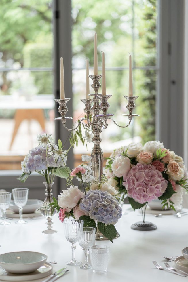 Stijlvol gedekte dinertafel met zilveren kandelaar en romantische bloemstukken in pasteltinten.