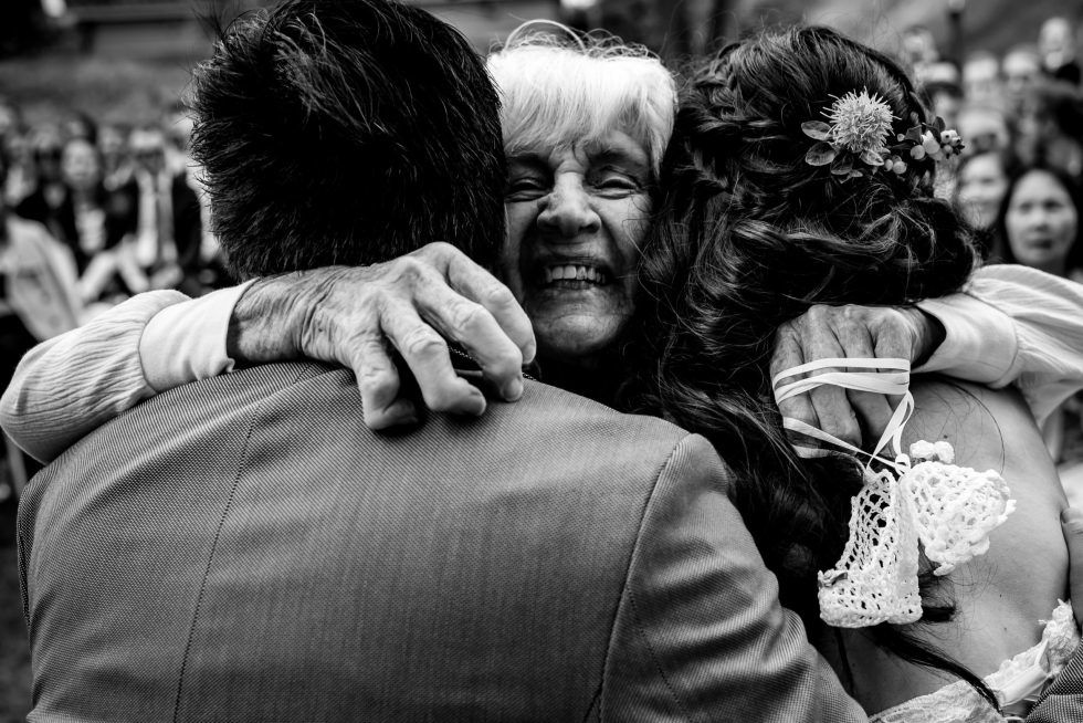 Blije grootmoeder omhelst pasgetrouwd stel vol liefde en trots tijdens bruiloftsreceptie.