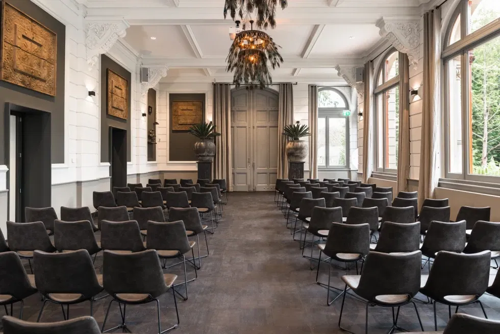 Stijlvolle trouwzaal in Oranjerie Hydepark met klassieke details, moderne stoelen en hoge ramen – elegante locatie voor ceremonie of huwelijksreceptie.
