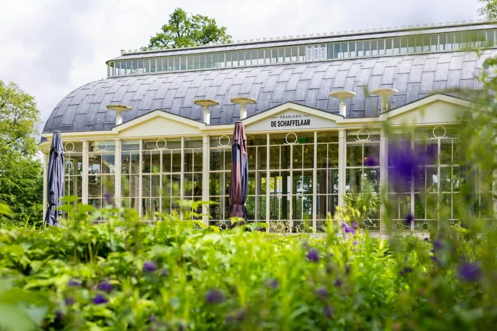 Vooraanzicht van Oranjerie De Schaffelaar met glazen gevel en bloeiende tuin – betoverende trouwlocatie midden in het groen van Barneveld.