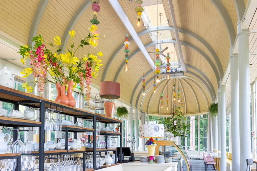 Sfeervol interieur van Oranjerie De Schaffelaar met kleurrijke lampen, servies op open rekken en bloemrijke accenten – unieke trouwlocatie met vrolijke ambiance.