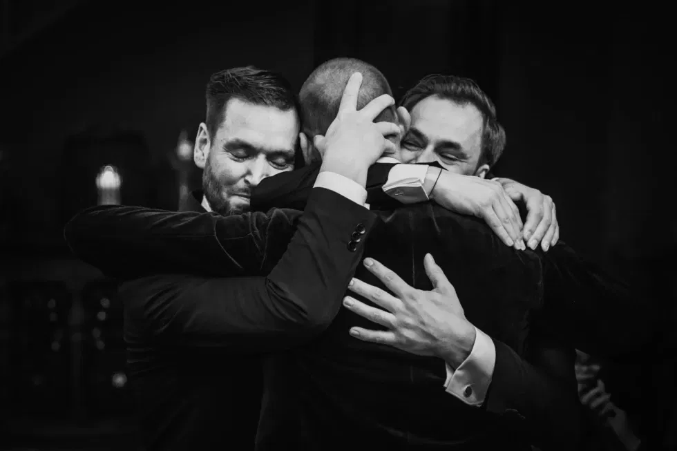 Emotionele omhelzing tussen drie mannen in smoking tijdens de bruiloft.