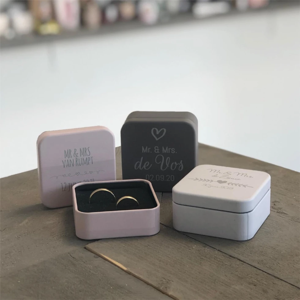 Gepersonaliseerde ringdoosjes met namen en trouwdata, stijlvol gepresenteerd op een houten tafel.