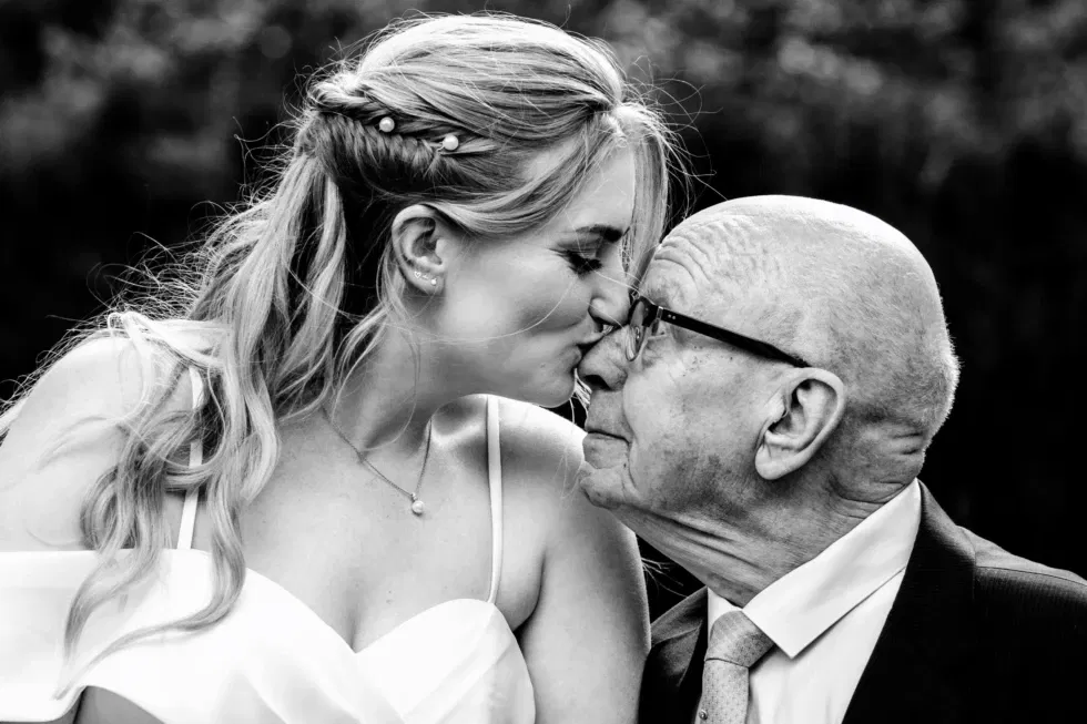 Bruid kust liefdevol haar grootvader op zijn neus in een teder moment op de trouwdag.