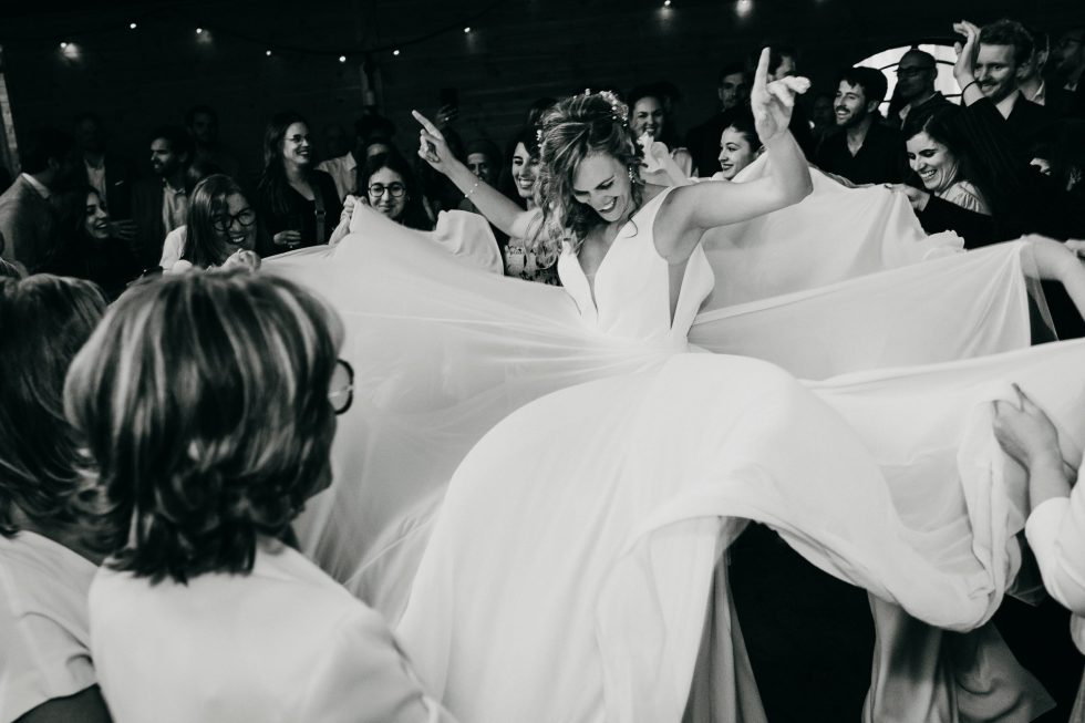 De jurk van de bruid wordt op het dansfeest omringd door gasten omhoog gehaald.