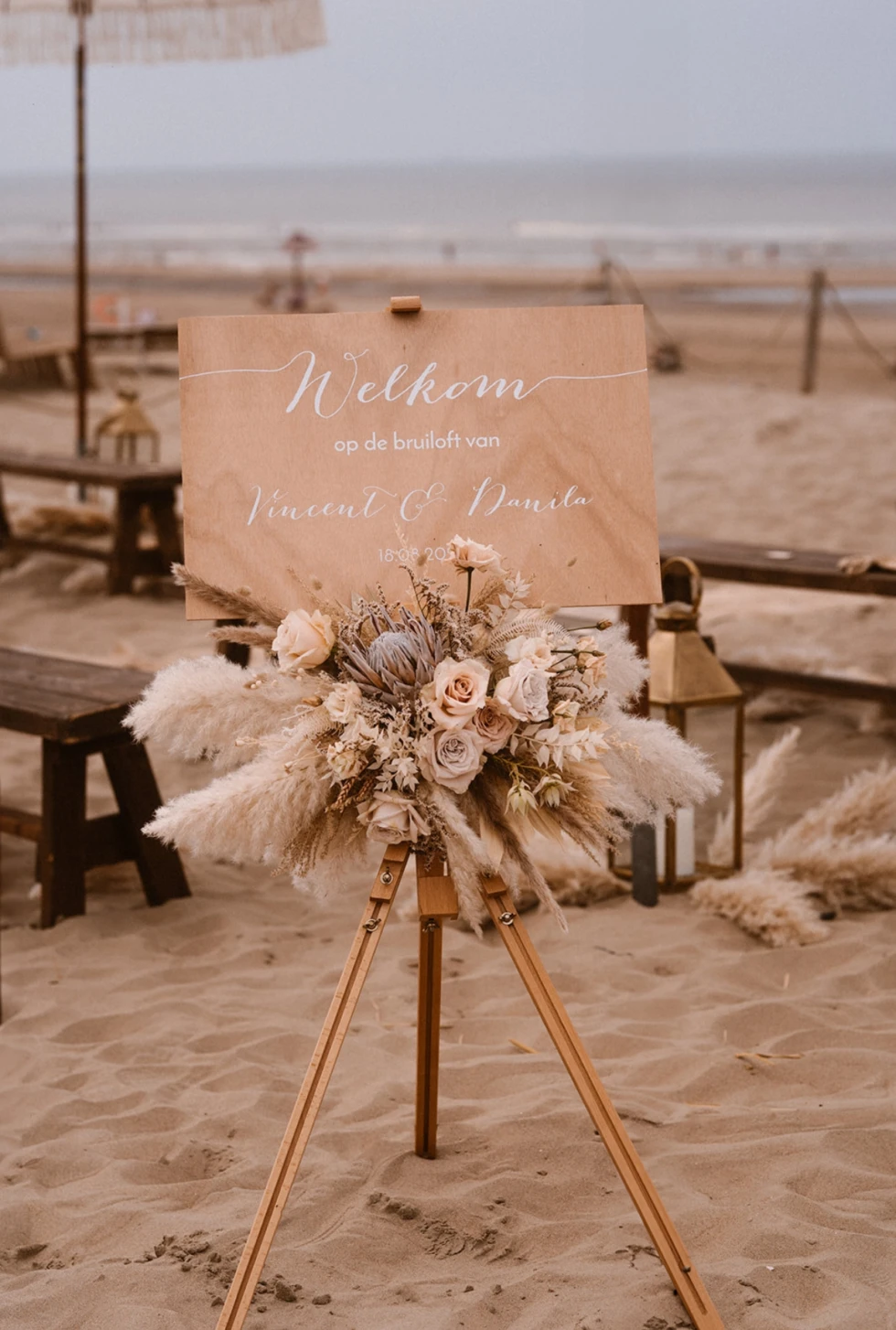 Houten welkomstbord met bloemenboeket op statief op het strand bij trouwceremonie.