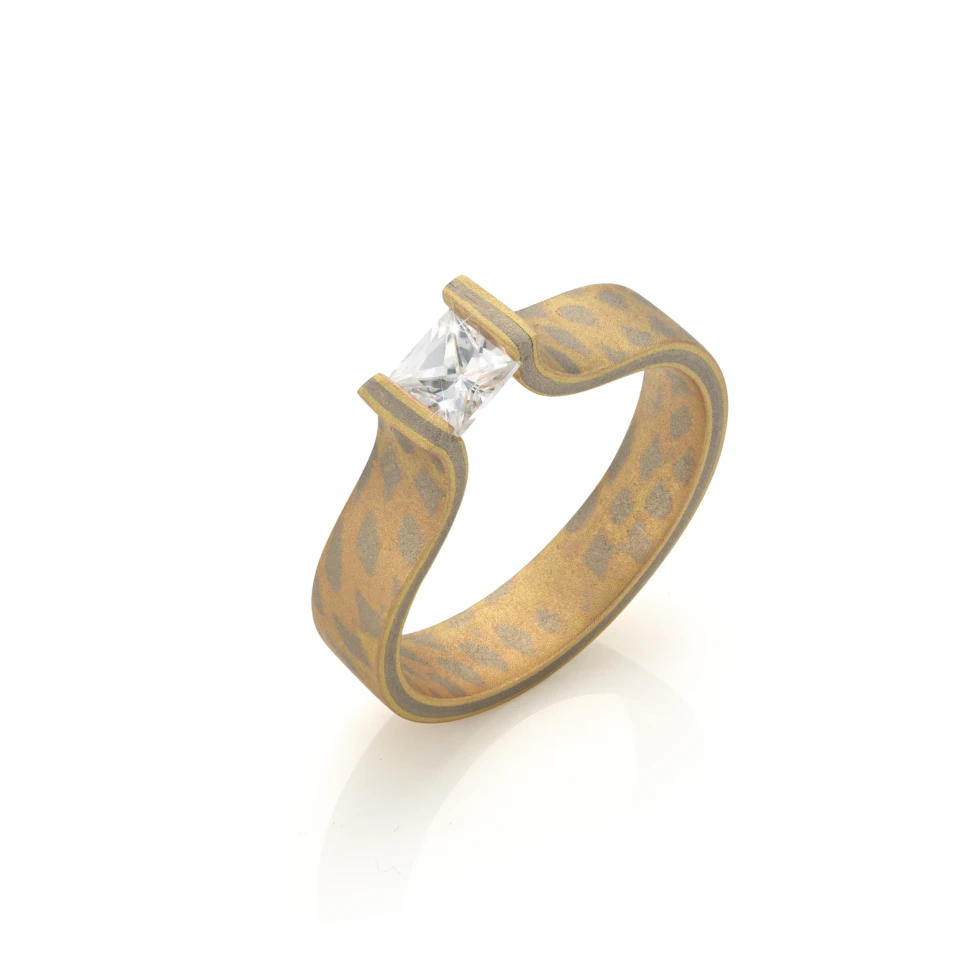Mokume gane verlovingsring met geometrisch patroon en vierkante diamant in moderne zetting.