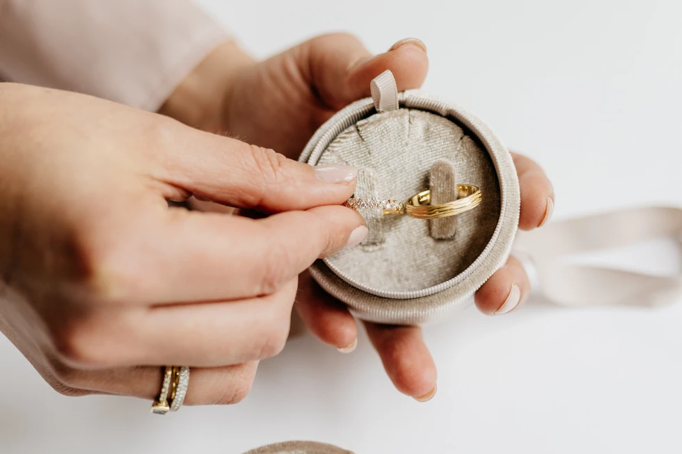 Hand plaatst diamanten ring naast gouden trouwring in luxe ringendoosje.