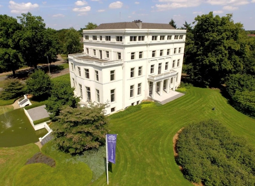 Luchtfoto van een statig wit herenhuis met verzorgde tuin en vijver, gelegen nabij het centrum van Zeist.