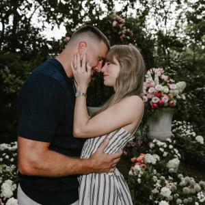 Een koppel kijkt elkaar liefdevol in de ogen en raakt met hun voorhoofden tegen elkaar. Ze omarmen elkaar in een tuin vol kleurrijke bloemen.