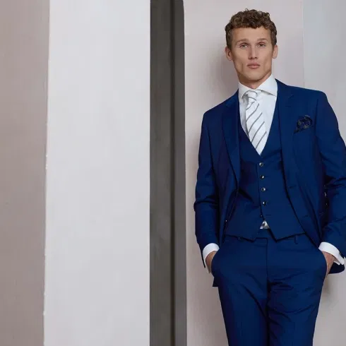 Bruidegom in donkerblauw trouwpak met stropdas en pochet tegen een neutrale achtergrond.