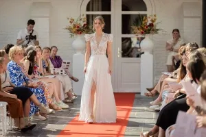 Vrouw loopt in een witte bruidsjurk over een rode loper waar allemaal mensen omheen zitten.