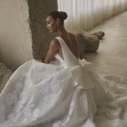 Romantische Casablanca trouwjurk met diepe V-rug, volumineuze rok en grote strikdetail, gefotografeerd in een elegante, minimalistische setting.