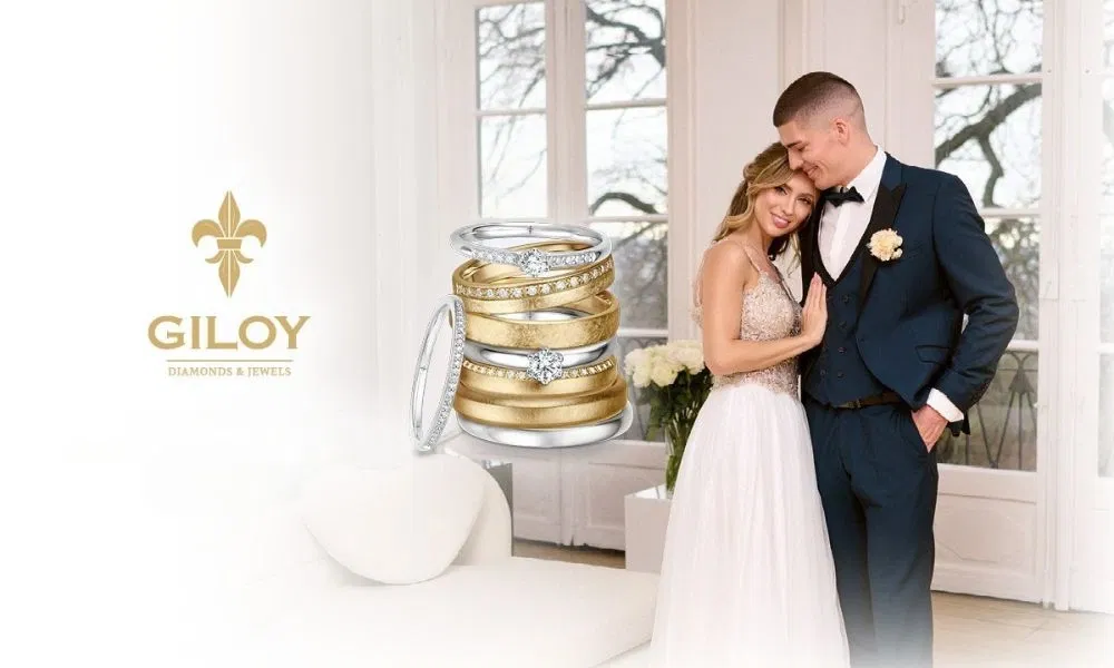 Bruidskoppel in trouwkleding poseert liefdevol naast een boeket witte rozen, met trouwringen van Giloy Diamonds & Jewels prominent in beeld.
